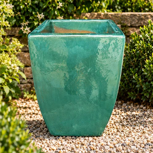 Square tapered planter with a glossy turquoise glazed finish set in a gravel garden